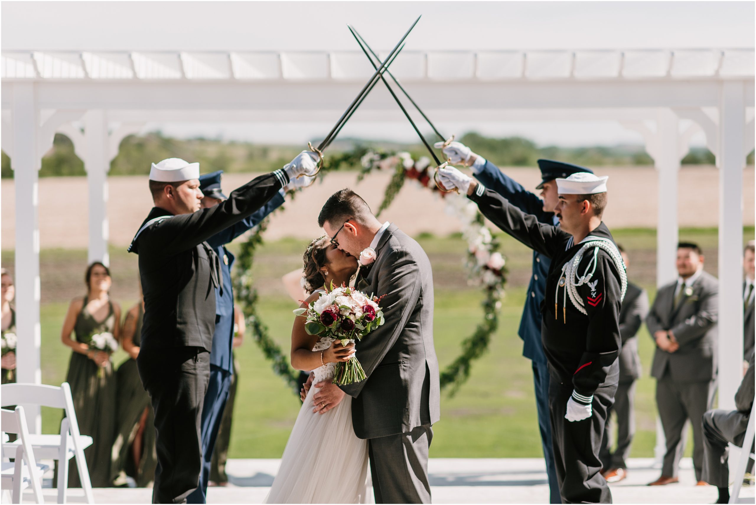 Bride and Groom kiss underneath and arch of swords outside at The Palace Event Center by Omaha Nebraska Photographer Anna Brace