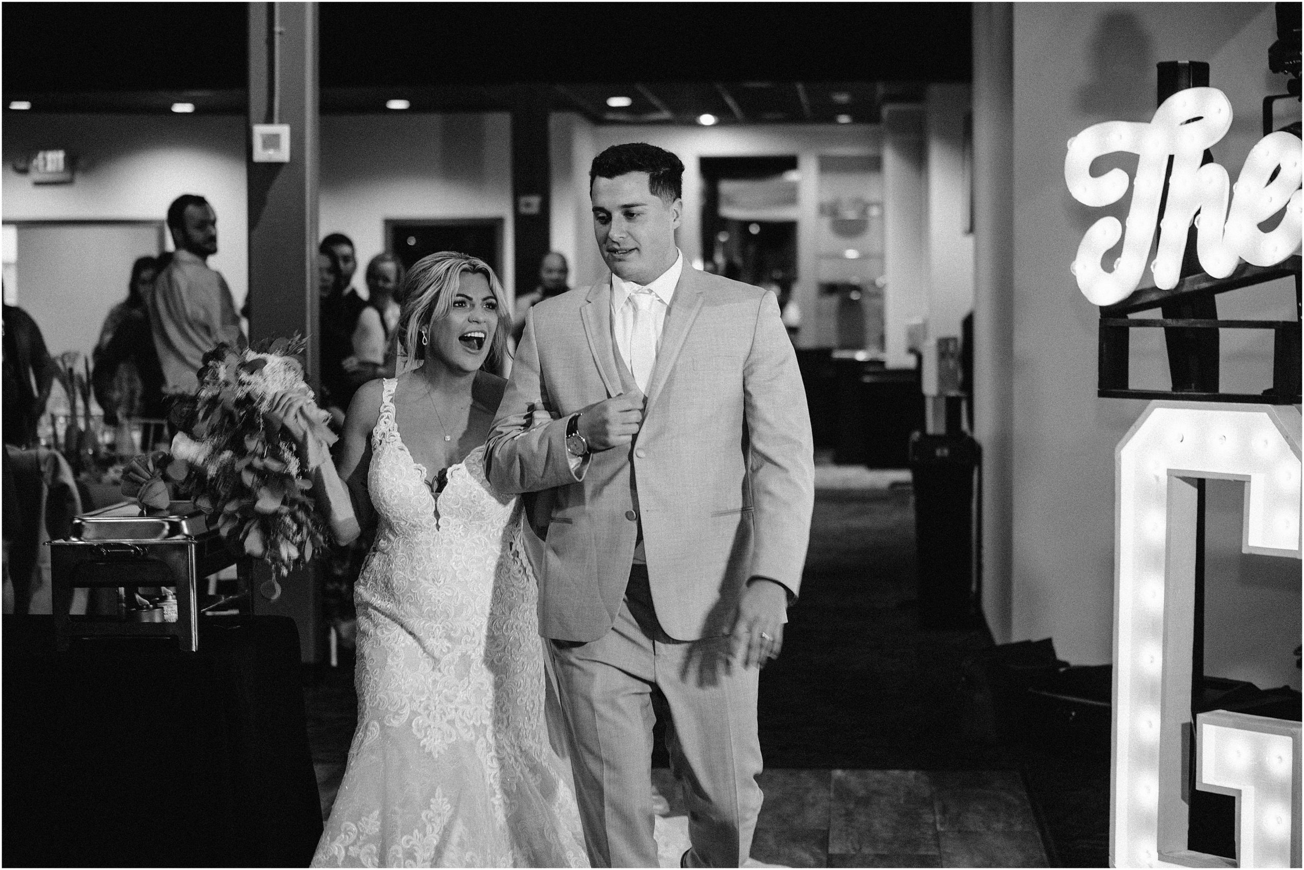 Bride and Groom hold hands and celebrate as they enter their wedding reception at the Soirée Room, an Omaha Nebraska Wedding Venue. Photo by Anna Brace who specializes in Omaha NE Wedding Photography