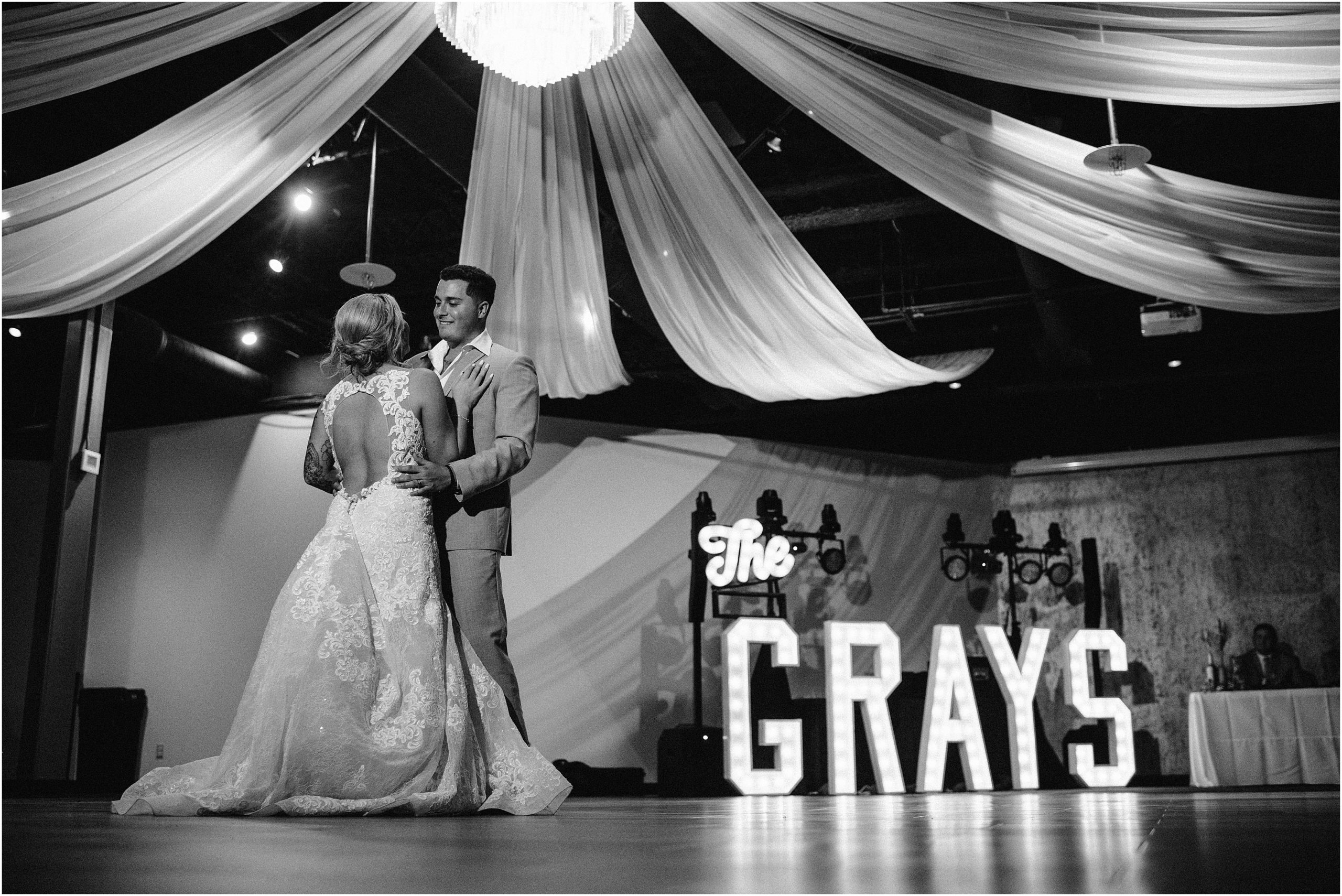 Black and White Photo of a Bride and Groom sharing their first dance at the Soirée Room, an Omaha Wedding Venue, with large Marquee letters in the background with their last name. Photo by Western Iowa Photographer, Anna Brace