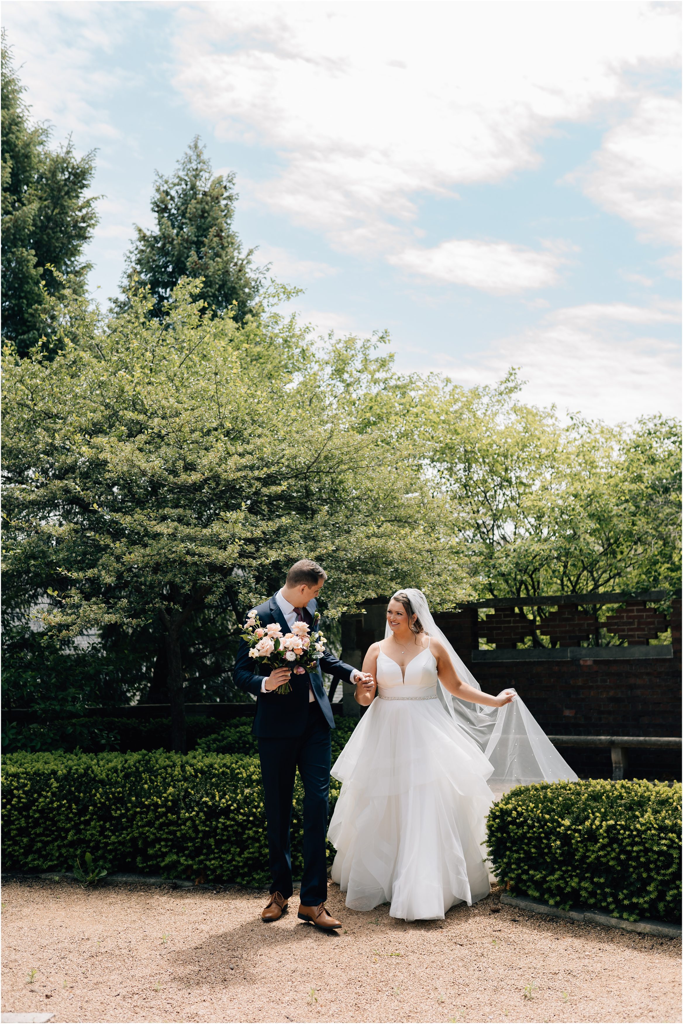 Bride and Groom walk hand in hand through the courtyard at Rollins Mansion in Des Moines Iowa. Photo by Anna Brace, an Omaha NE wedding photographer.