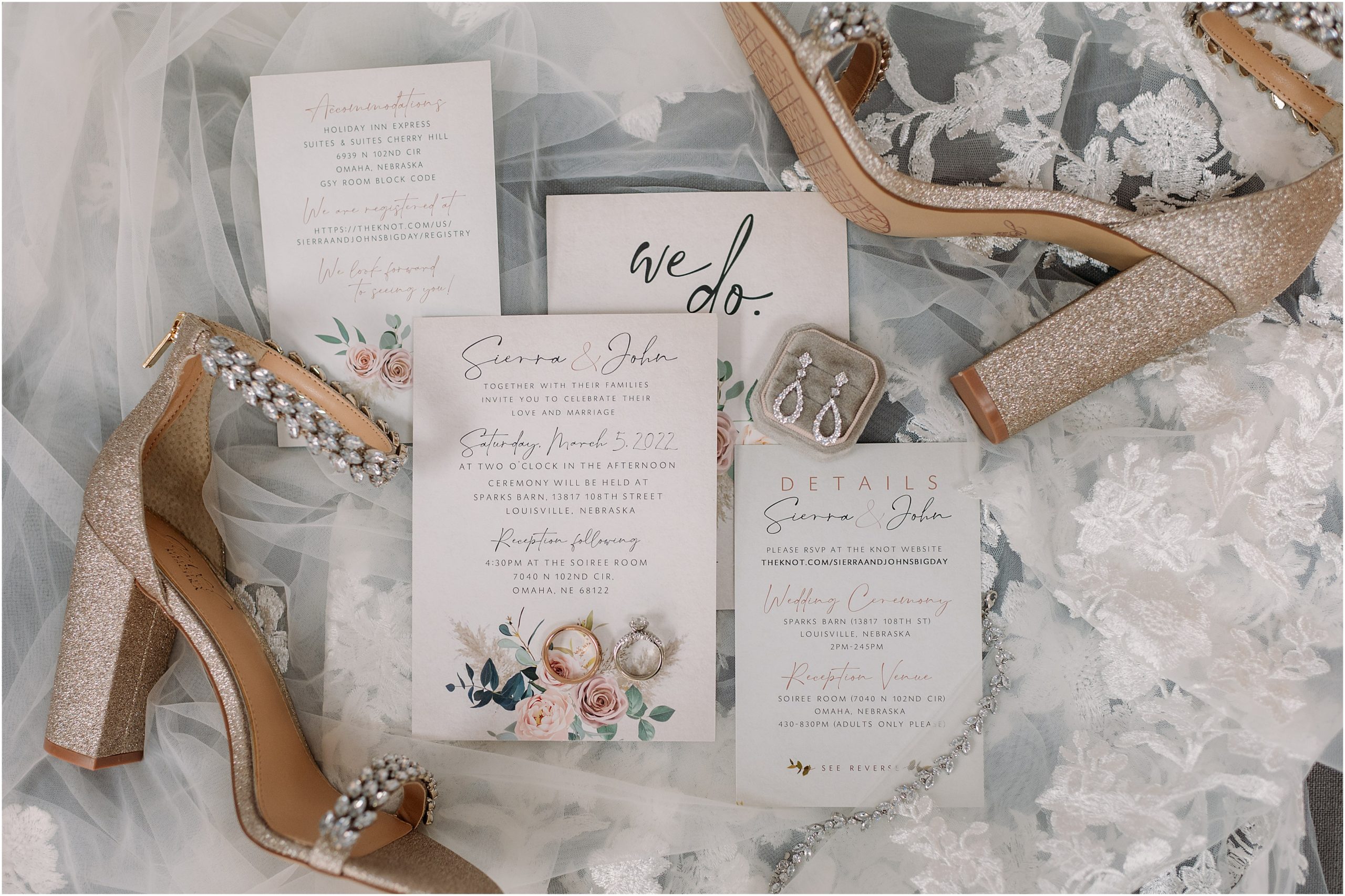Floral wedding invitation, diamond ring and earrings, sparkly gold heels, all lay on top of a cathedral length floral lace wedding veil at the Soirée Room, an Omaha Wedding Venue, taken by Omaha wedding photographer, Anna Brace