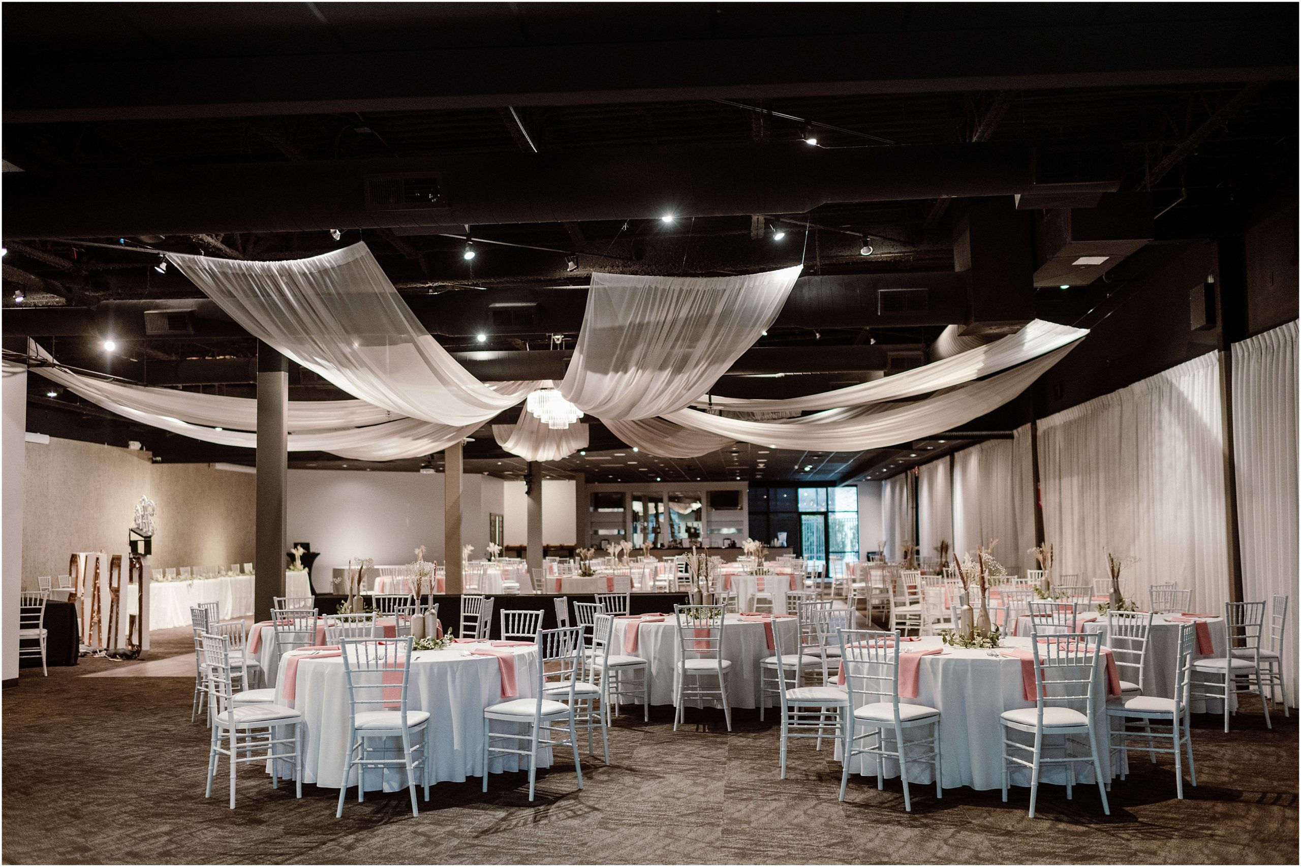 A wide view of The Soiree Room in Omaha, showing all the white tables and chairs with pink accents. Taken by Omaha NE Wedding Photographer, Anna Brace