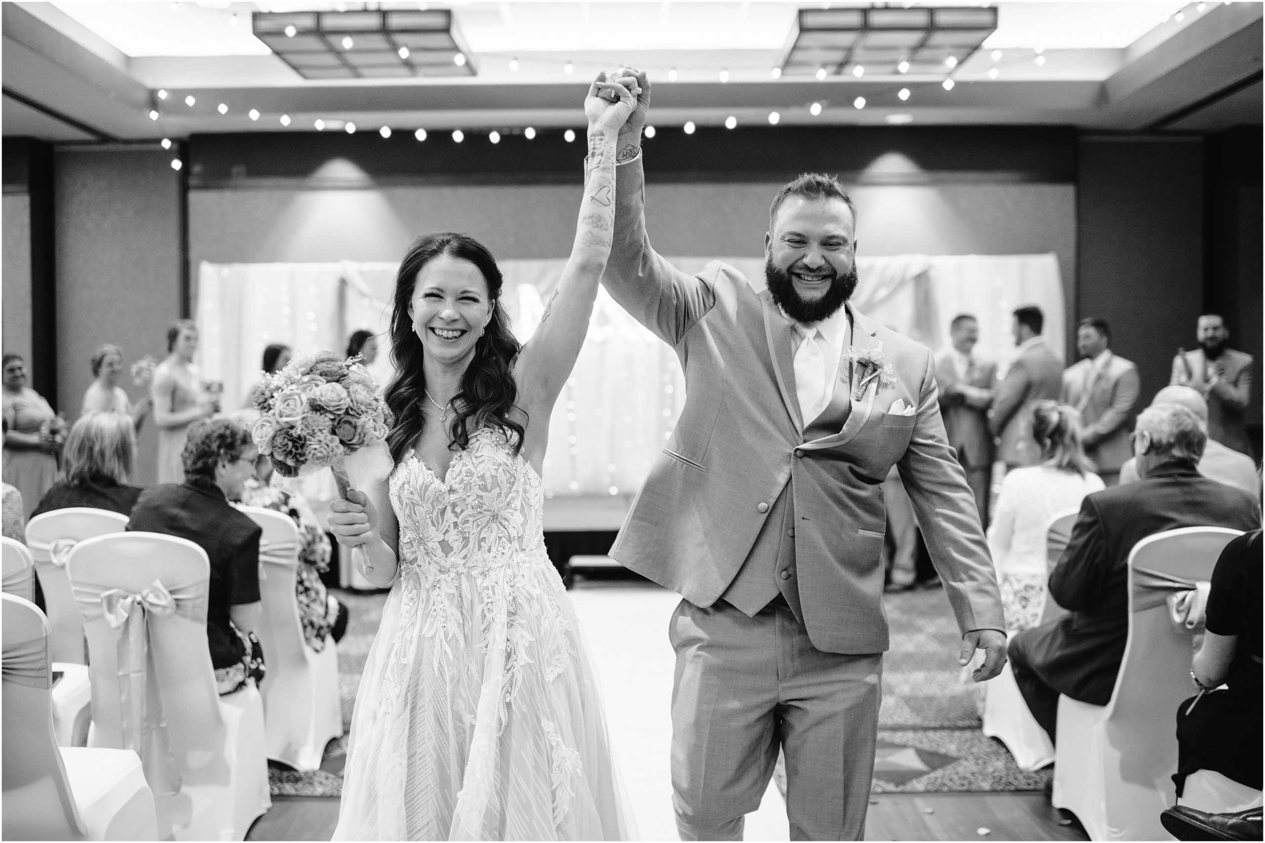 Black and white photo of bride and groom sharing a fist pump after getting married while walking down the aisle at their Honey Creek Resort wedding on Rathbun lake. Photo by Anna Brace, an Omaha NE wedding Photographer.