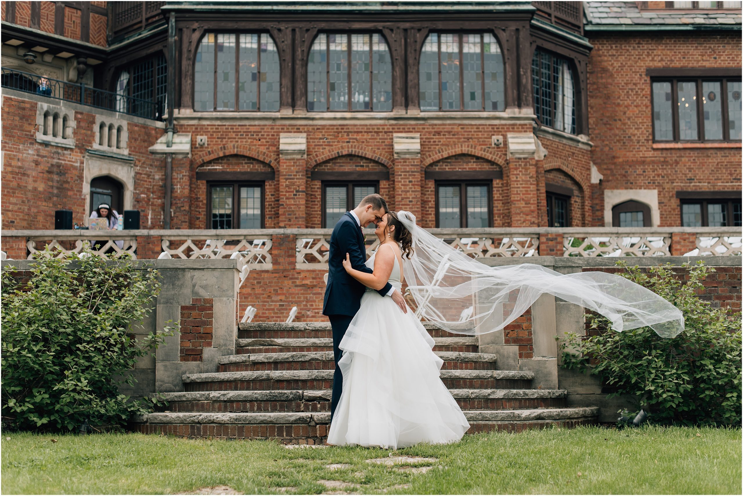 Bride and Groom talk while the bride's long veil blows in the wind in front of Rollins Mansion. Photo by Anna Brace who specializes in Omaha Nebraska Photographer.