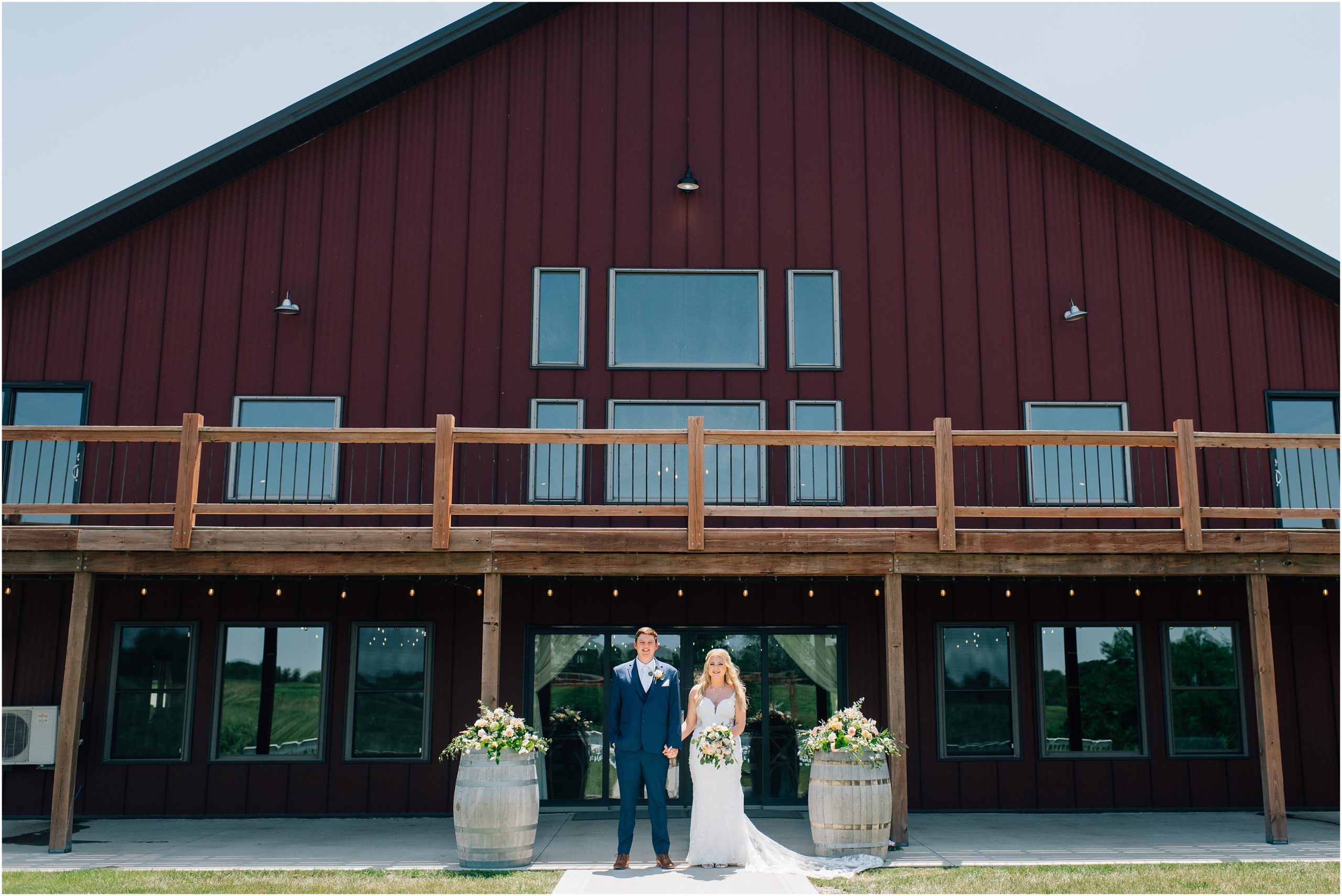 Bride and Groom stand hand in hand in front of the red barn venue, Carper Vineyard and Winery, a wedding venue near des moines. Photo by Anna Brace, who specializes in Omaha Wedding Photography