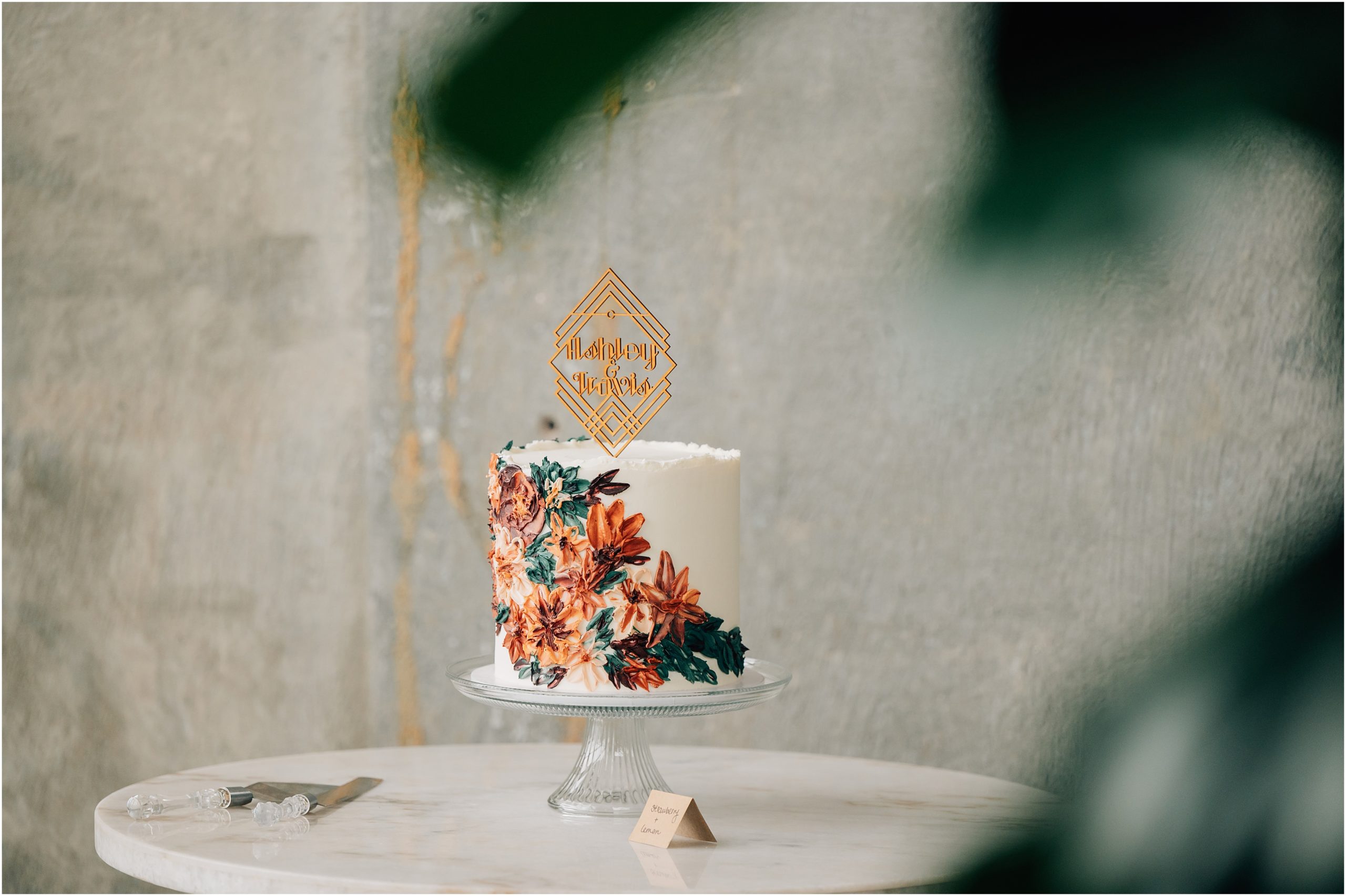 Buttercream painted wedding cake with oranges, peaches, green leaves. This Fall floral wedding cake is set up at the Omaha Wedding Venue, Cafe Postale. Photo by Anna Brace, a wedding photographer in Omaha. 