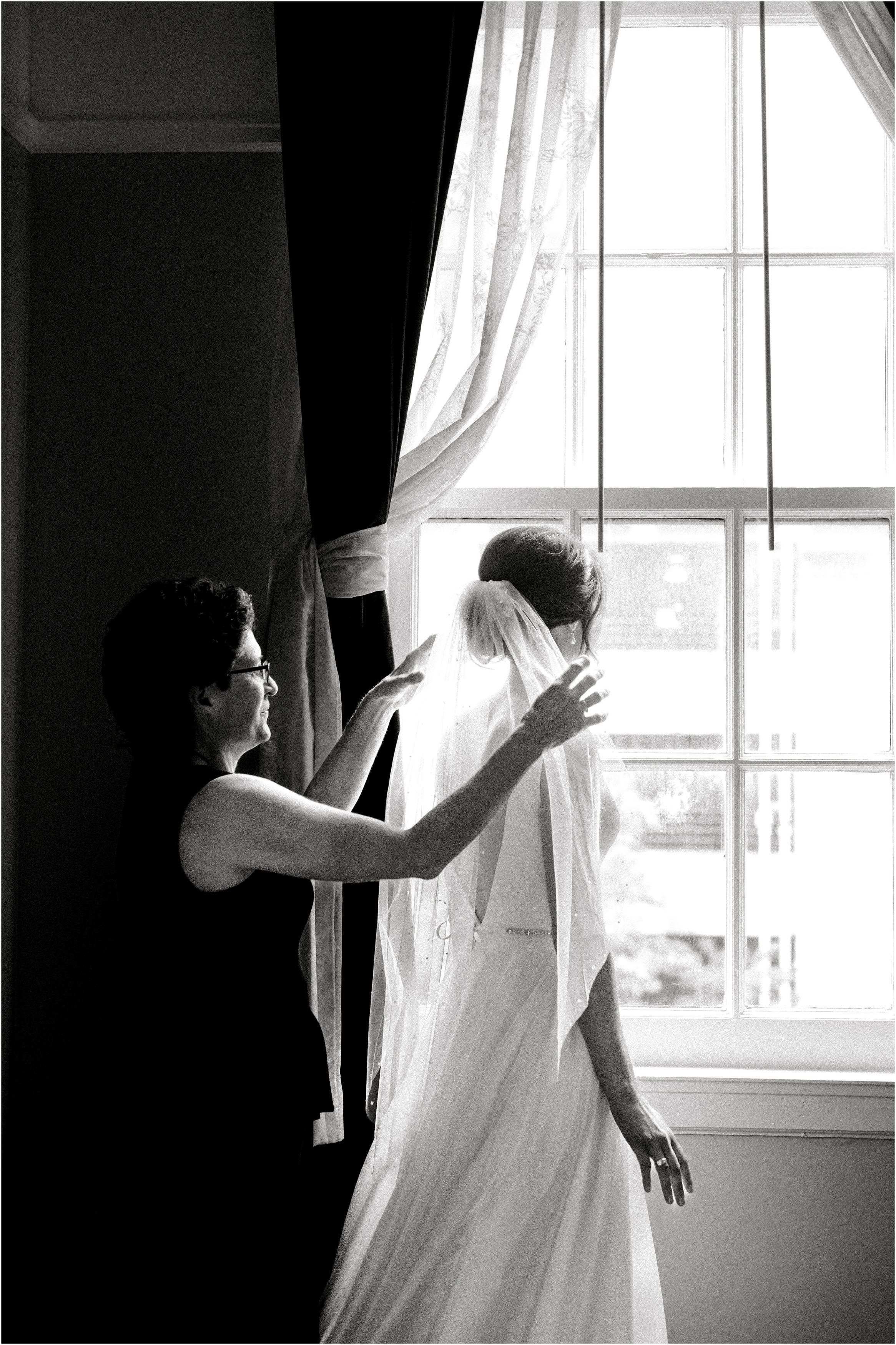 Bride's mother adjusts her veil in front of a window at the Omaha Wedding Venue, Magnolia Hotel. Photo by Omaha NE wedding Photographer, Anna Brace.
