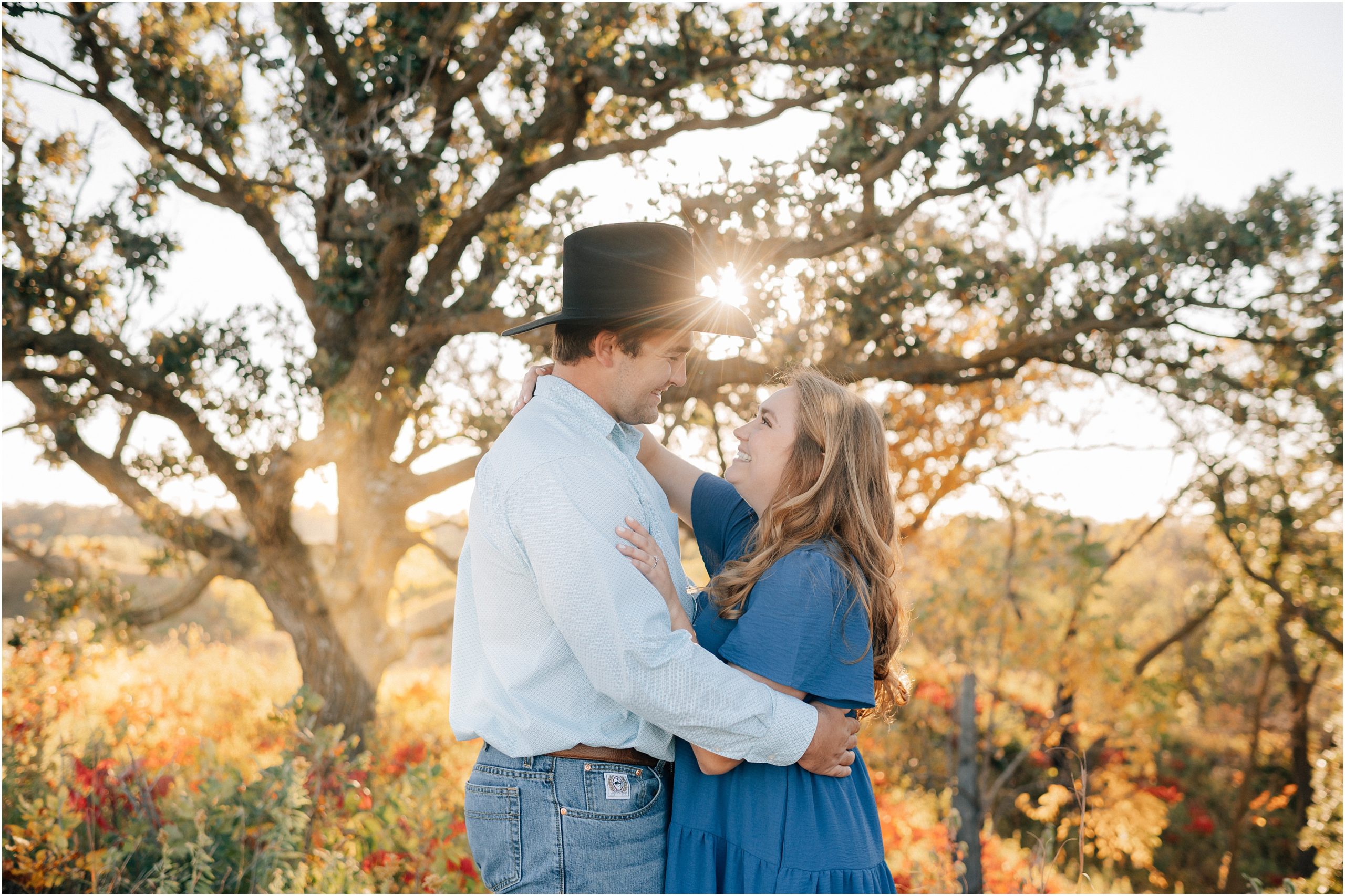 A cowboy and his fiance smile at each other while the sun peaks through his hat at their Hitchcock Nature Center engagement session. Photos by Anna Brace, an Omaha wedding photographer. 