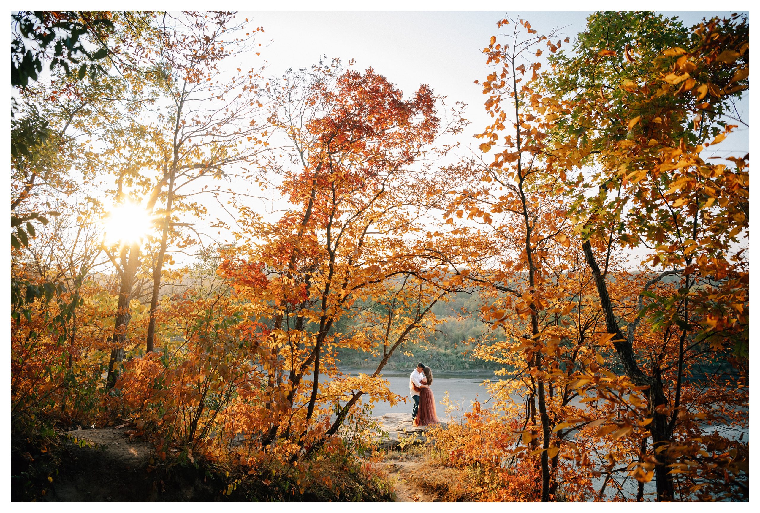 An engaged couple hugs while standing on a ledge surrounded by colorful fall trees at their Engagement Photos at Ledges State Park. Photos are by Anna Brace, a wedding photographer in Des Moines. 