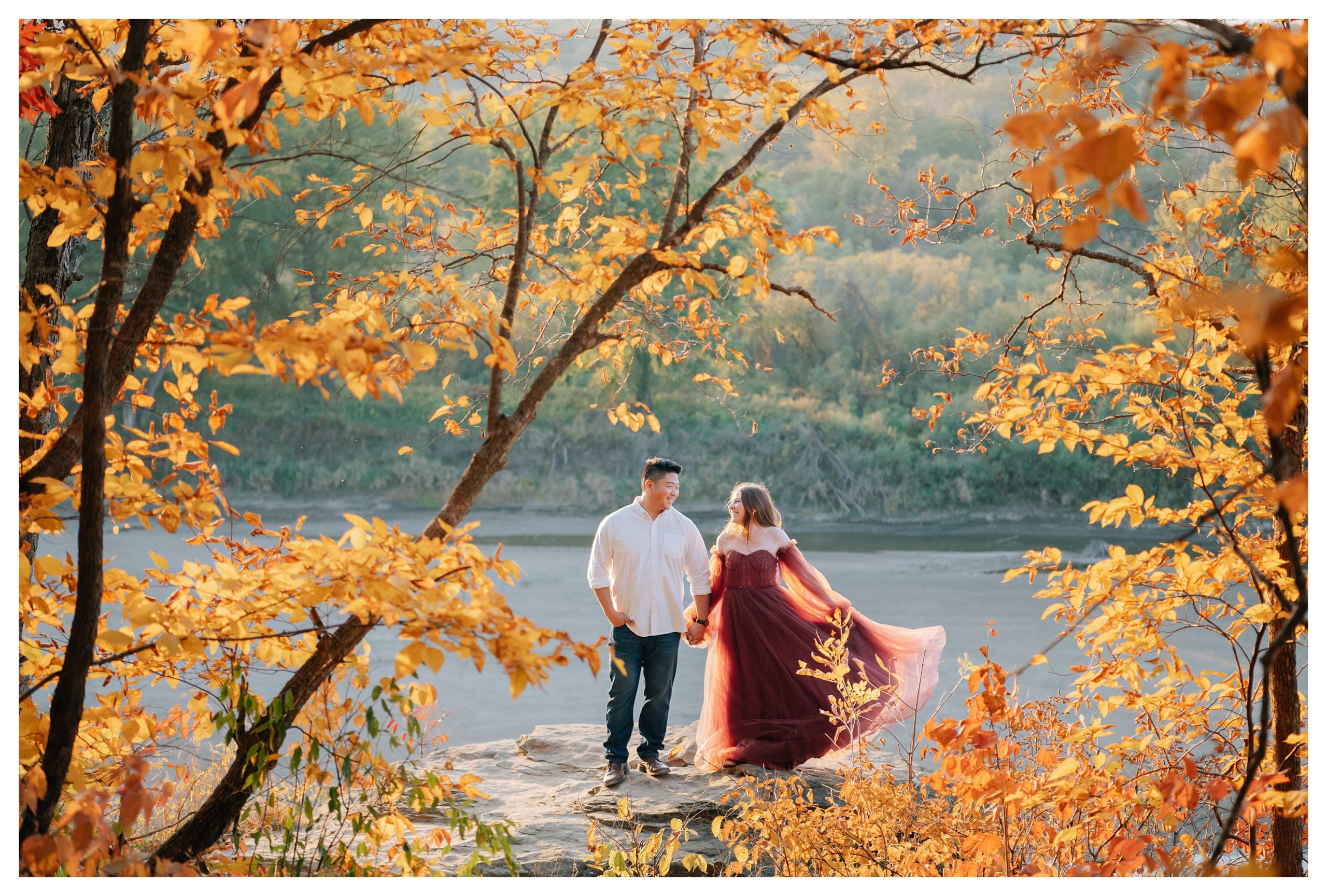 A Man wearing white shirt and jeans and his fiance wearing a rusty red floor length gown get their engagement photos taken in the fall at Ledges State Park by Anna Brace, a Des Moines wedding photographer. 