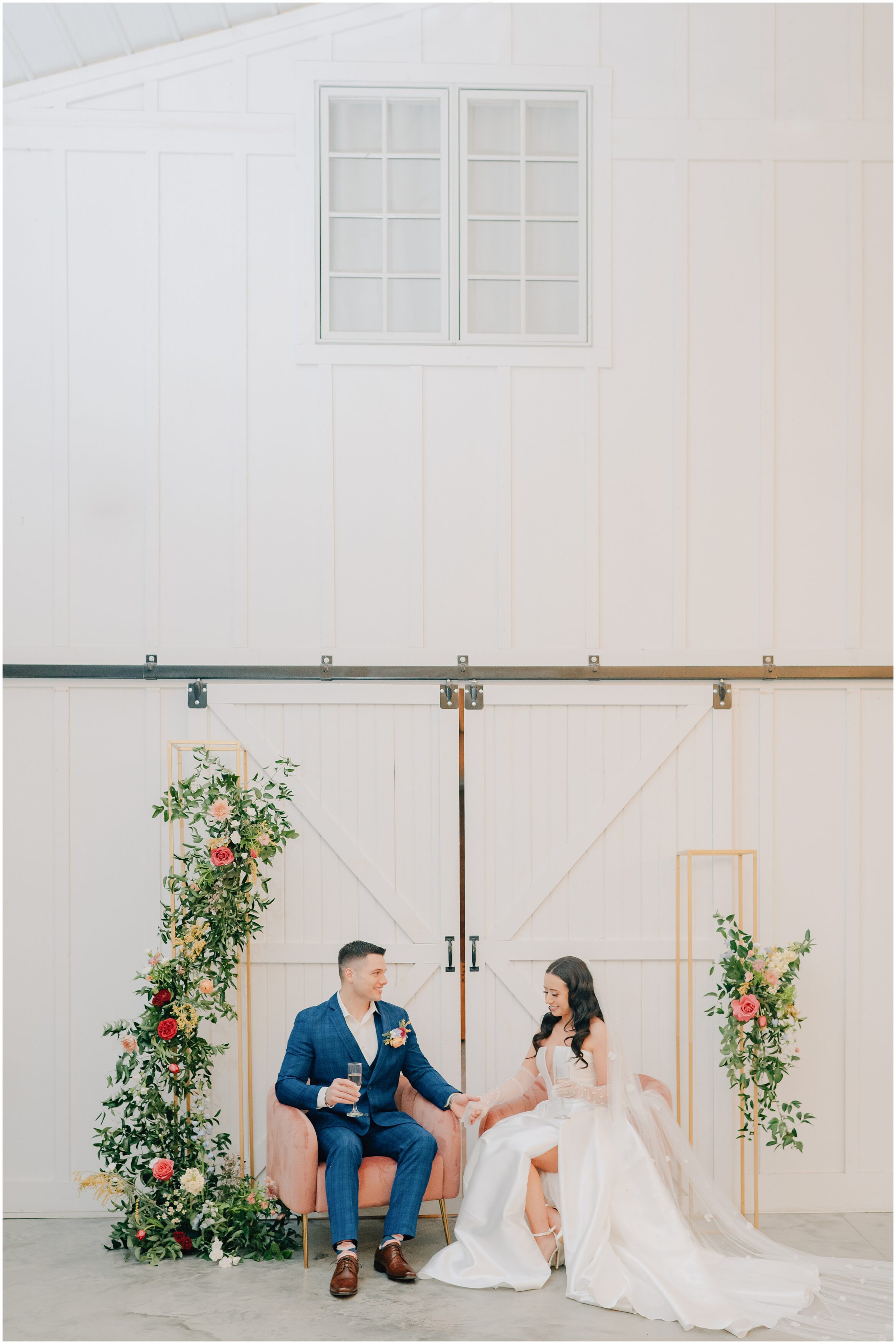 Bride and Groom sit in front of a spring floral backdrop at Magnolia Farms, a wedding venue in Iowa. Photo taken by Anna Brace, an Iowa Wedding Photographer
