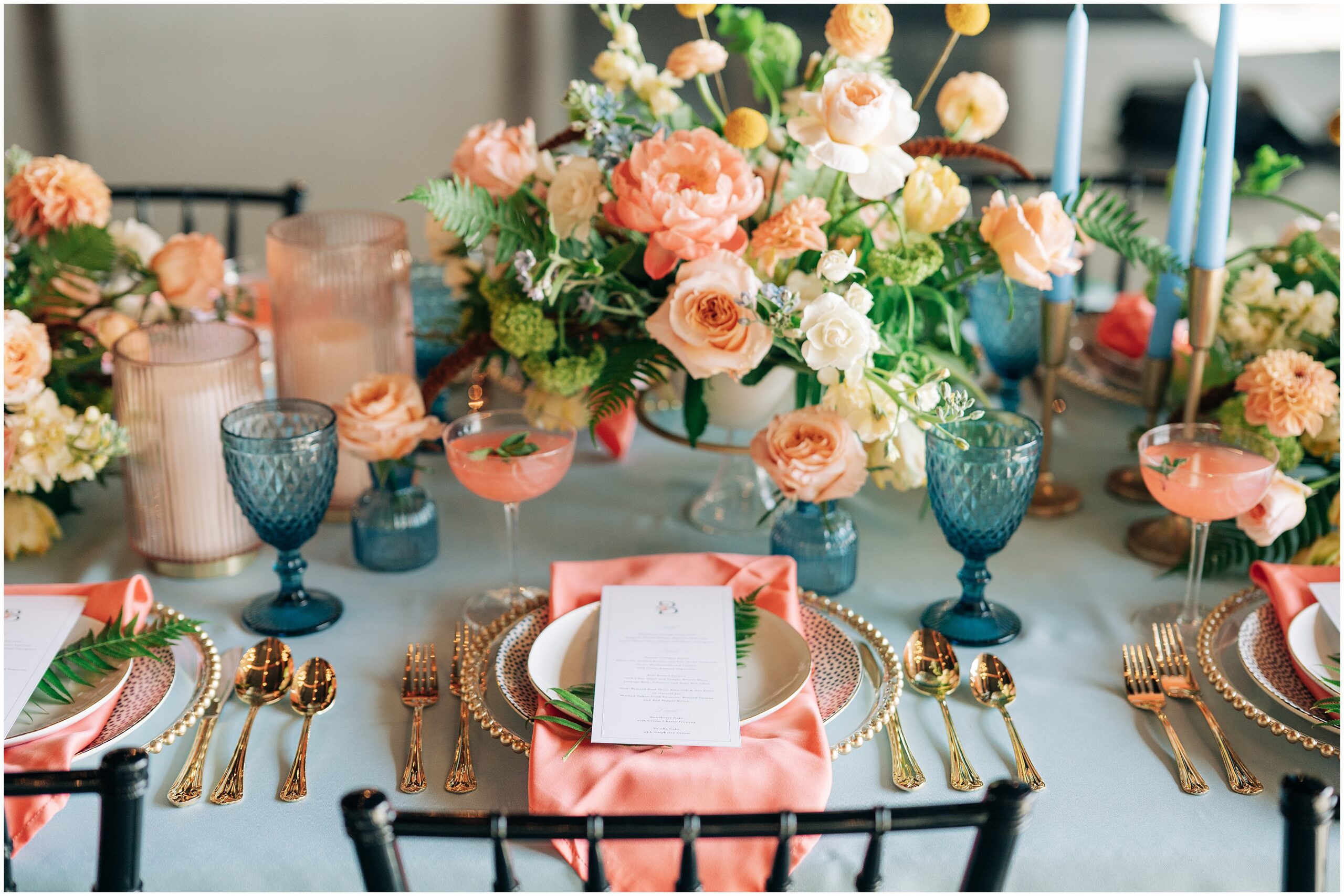 Blue tablecloth, gold silverware, peach napkins, and peach yellow dusty blue and greenery bouquet by Lavish Floral Design set up by White Linen Planning. Photo by Anna Brace an Omaha wedding photographer.