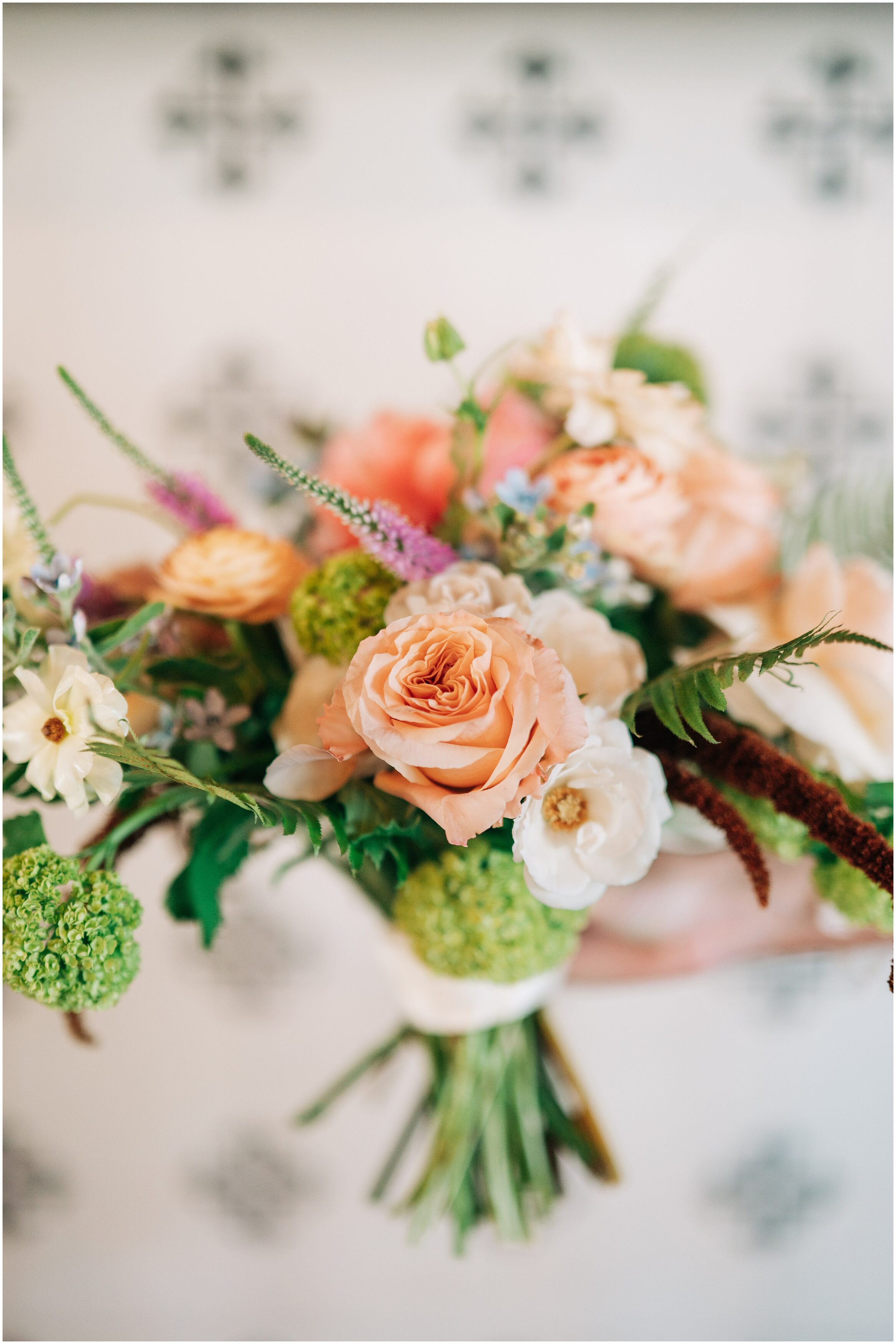 Lavish Floral Design created a beautiful spring bouquet with roses, ranunculus,  ferns, and other colorful florals for a spring wedding. Photo by Anna Brace, an Omaha Nebraska Wedding Photographer.