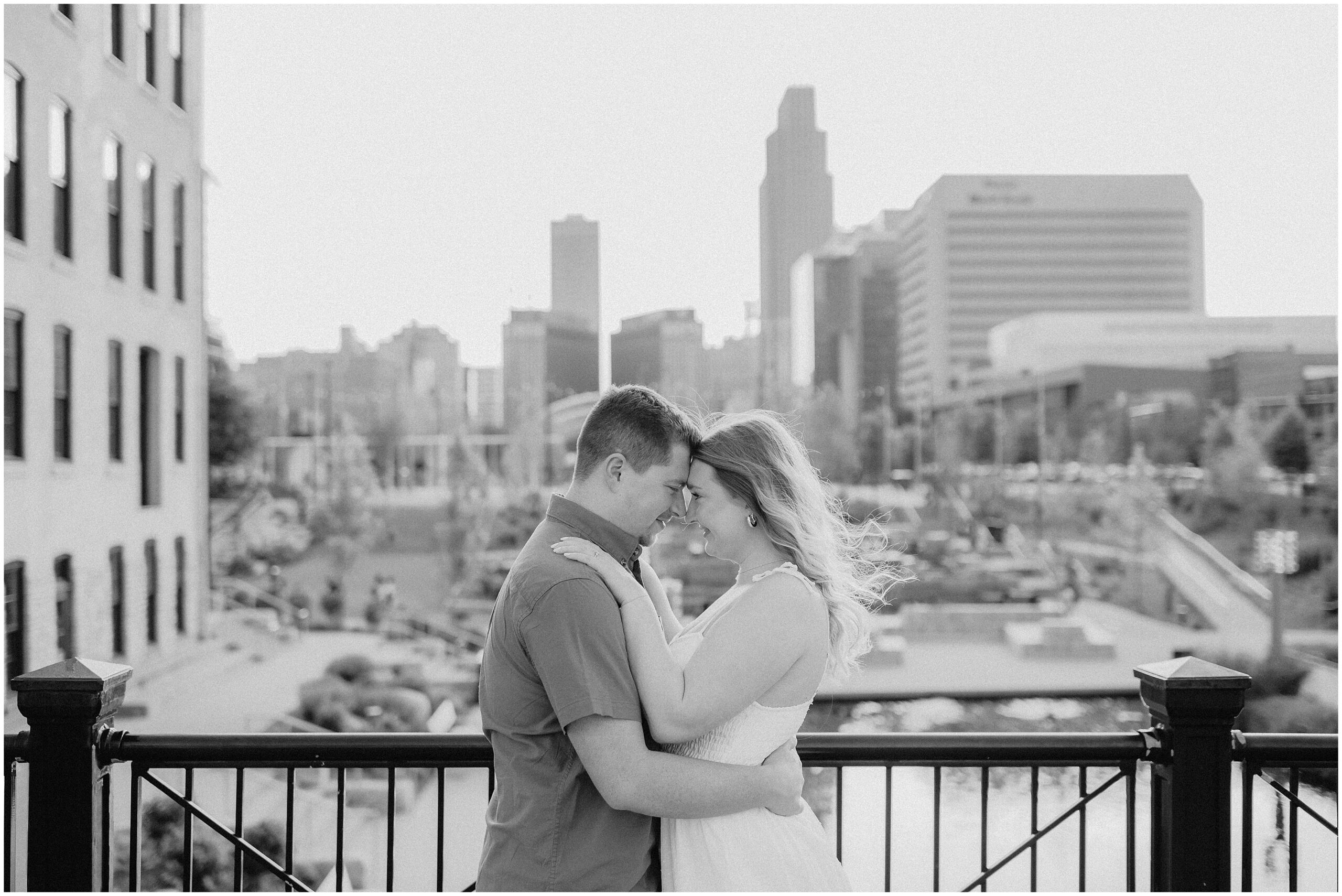 Engaged couple smiles at each other with Gene Leahy Mall in the background. By Omaha engagement photographer, Anna brace.