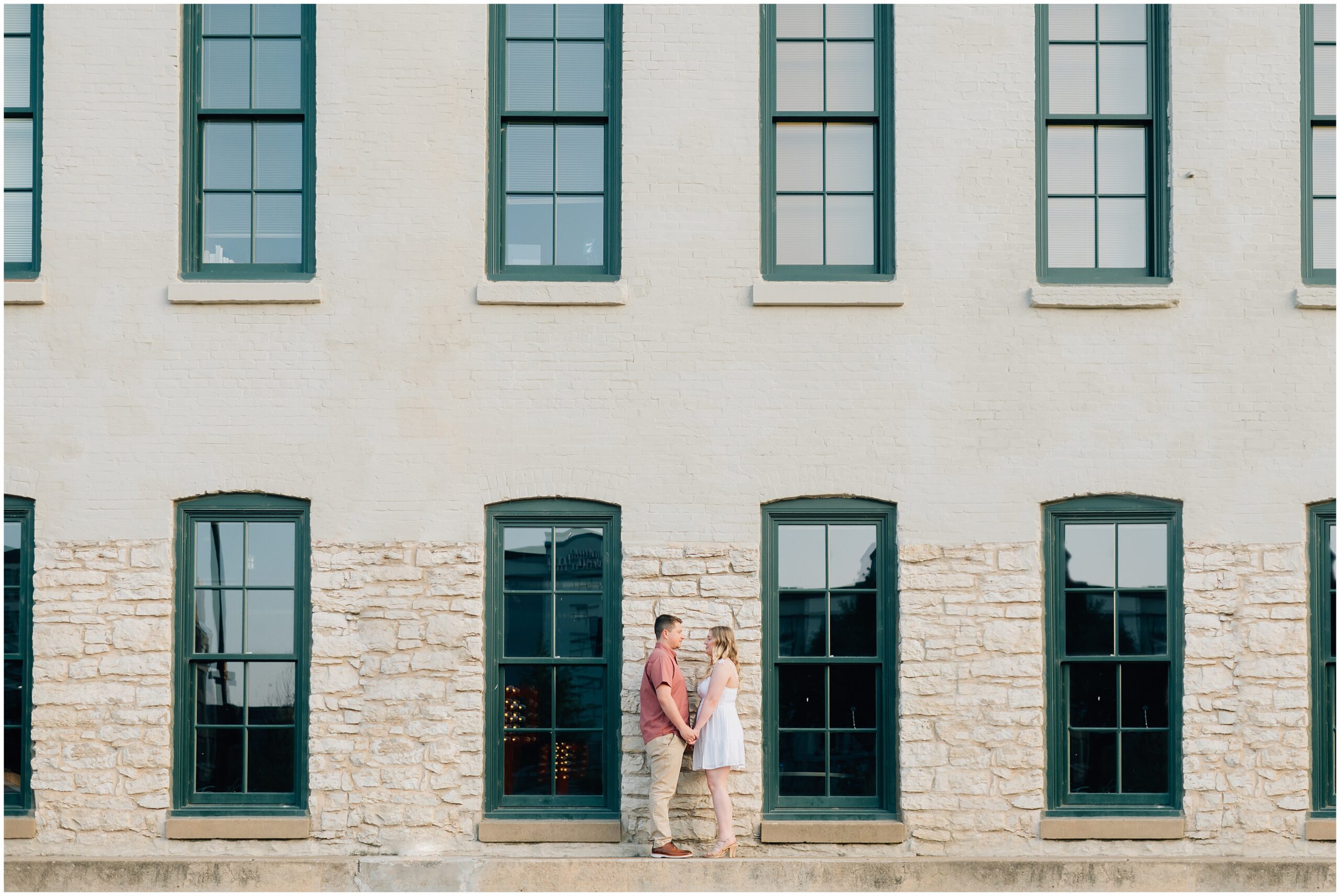 Engaged couple stands in front of a building at Gene Leahy Mall. Photo by Anna Brace, an Omaha wedding photographer.